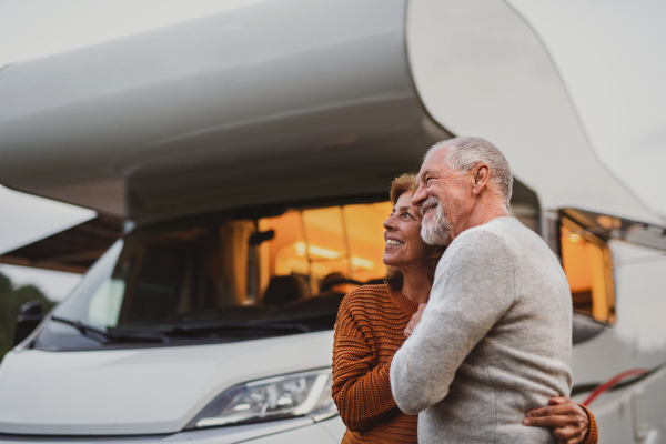 A senior couple standing and hugging outdoors at dusk, caravan holiday trip.