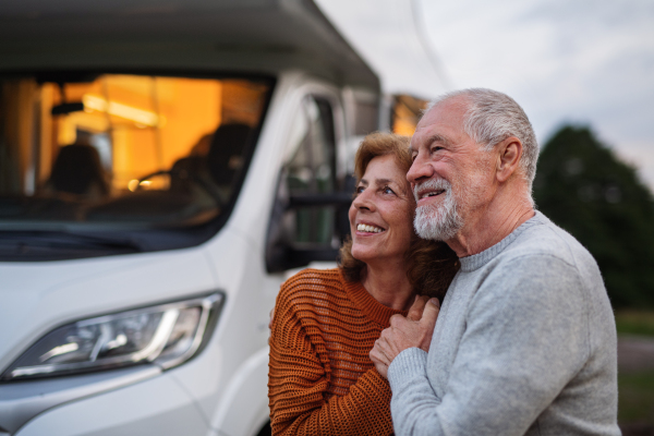 A senior couple standing and hugging outdoors at dusk, caravan holiday trip.