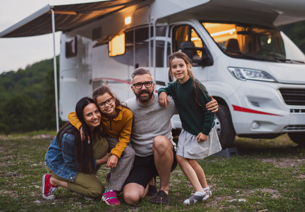 Front view of happy family looking at camera outdoors at dusk, caravan holiday trip.