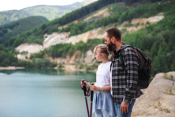 A happy preteen girl with father on hiking trip on summer holiday, looking at lake scenery.