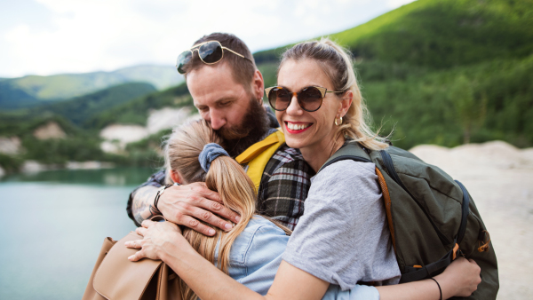 A happy family with preteen daughter on hiking trip on summer holiday, resting and hugging.