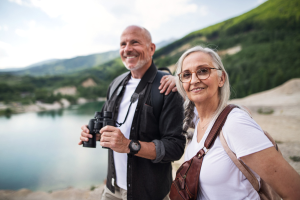 A happy senior couple on hiking trip on summer holiday, using binoculars.