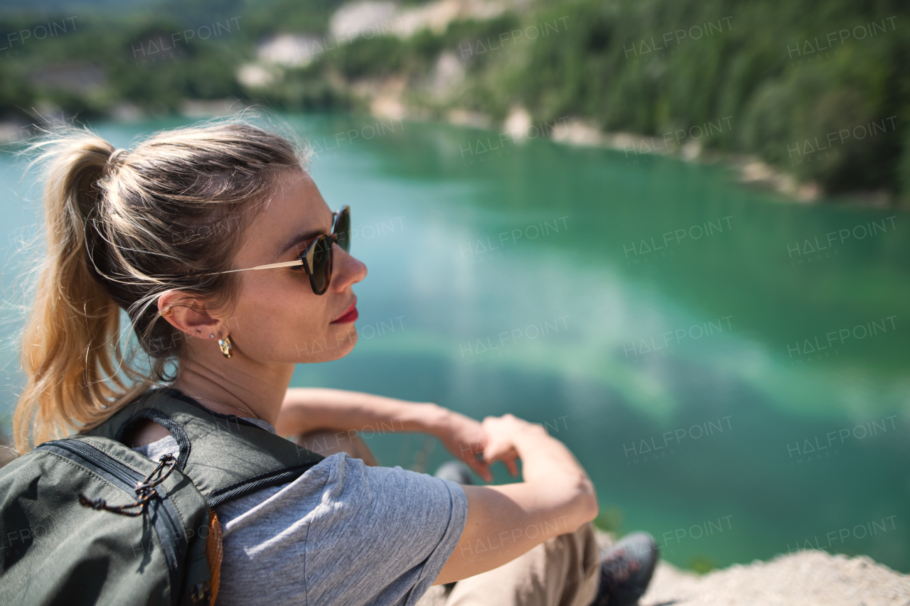 A mid adult woman tourist on hiking trip on summer holiday, resting by lake.