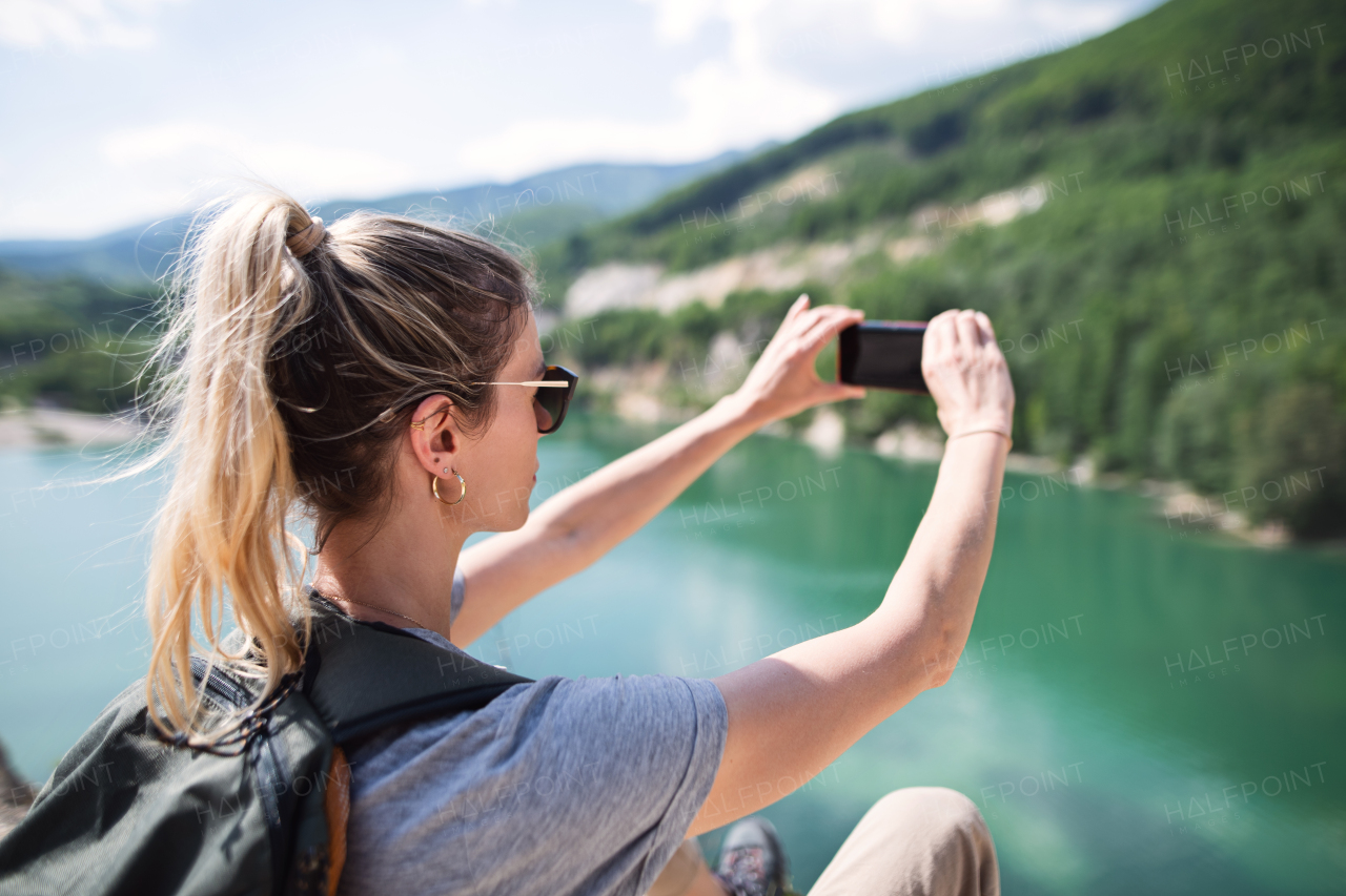 A mid adult woman tourist on hiking trip on summer holiday, taking photograph with smartphone.