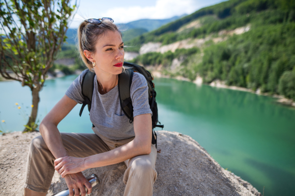 A mid adult woman tourist on hiking trip on summer holiday, resting by lake.