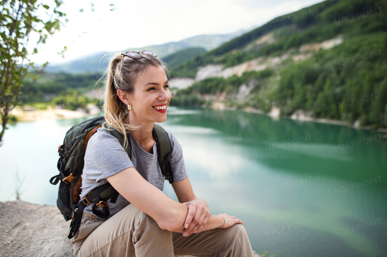 A mid adult woman tourist on hiking trip on summer holiday, resting by lake.