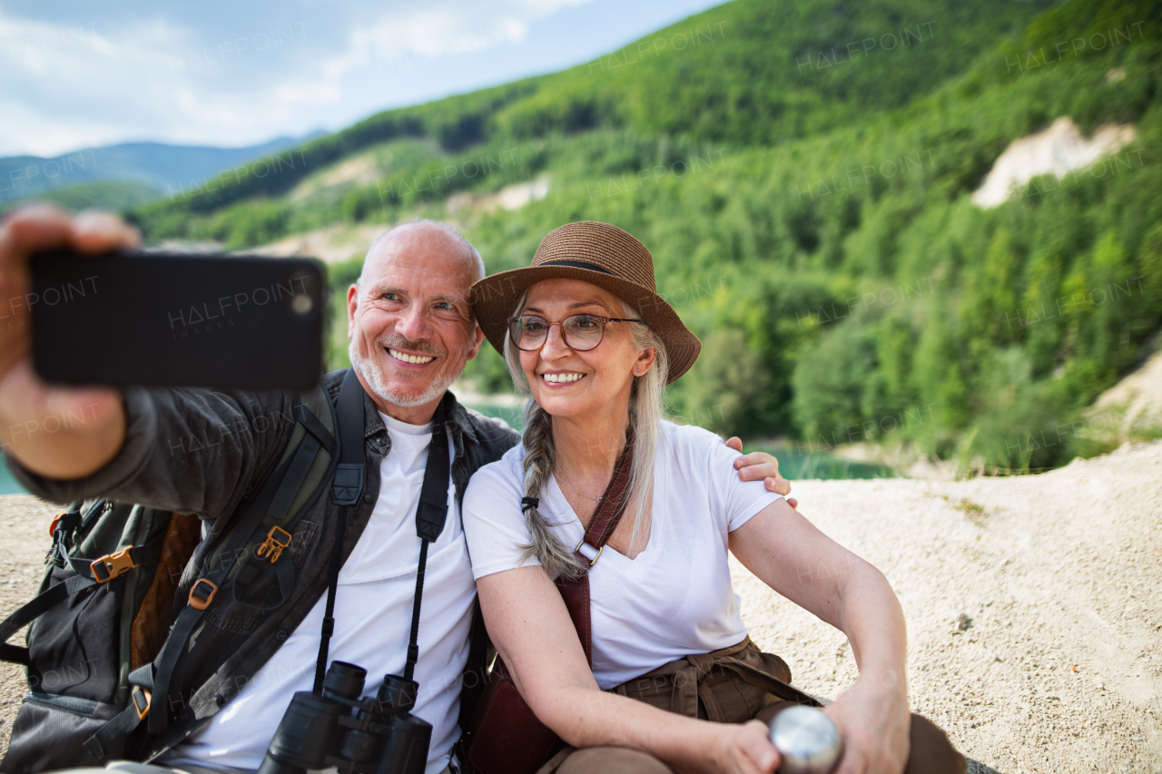 A happy senior couple on hiking trip on summer holiday, taking selfie.