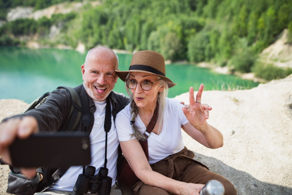 A happy senior couple on hiking trip on summer holiday, making faces when taking selfie.