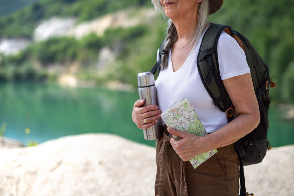 Midsection of unrecognizable senior woman tourist on hiking trip on summer holiday, standing by lake.