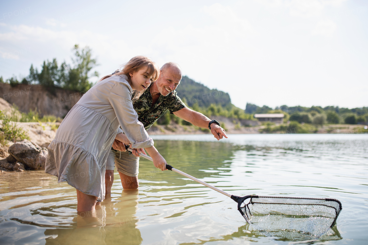 Happy preteen girl and senior grandfather with fishing net on summer holiday by lake.