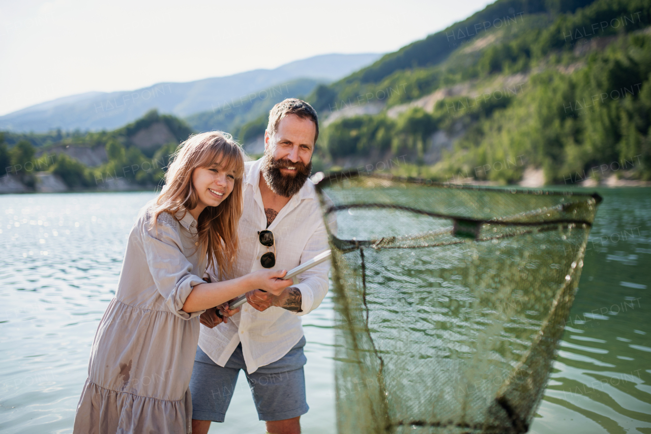 Happy preteen girl and mature father with fishing net on summer holiday by lake.