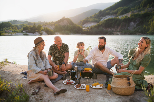 A happy multigeneration family on summer holiday trip, barbecue by lake.