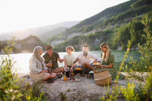 A happy multigeneration family on summer holiday trip, barbecue by lake.