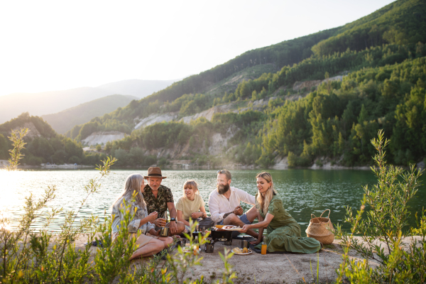 A happy multigeneration family on summer holiday trip, barbecue by lake.