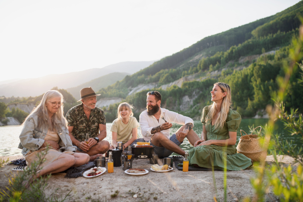 A happy multigeneration family on summer holiday trip, barbecue by lake.