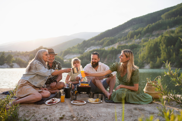 A happy multigeneration family on summer holiday trip, barbecue by lake.