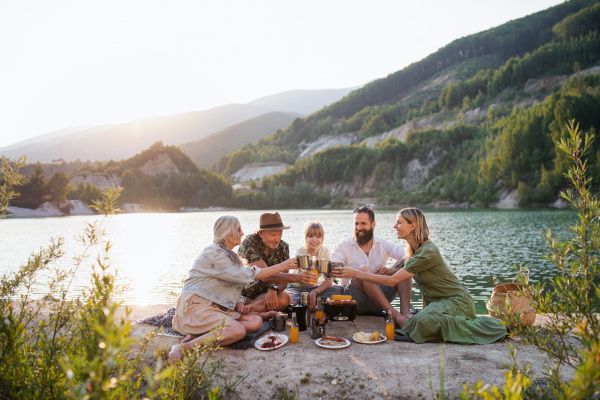 A happy multigeneration family on summer holiday trip, barbecue by lake.