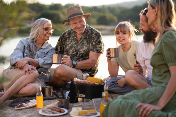 A happy multigeneration family on summer holiday trip, barbecue by lake.