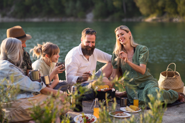 A happy multigeneration family on summer holiday trip, barbecue by lake.