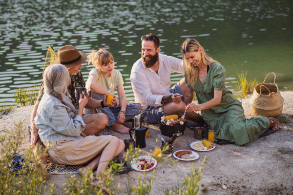 A happy multigeneration family on summer holiday trip, barbecue by lake.