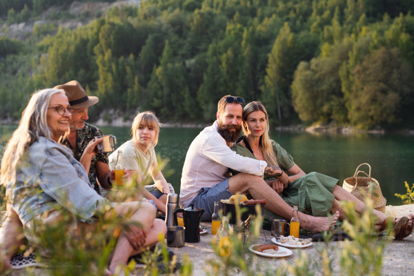 A happy multigeneration family on summer holiday trip, barbecue by lake.