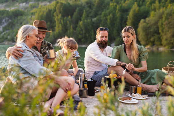 A happy multigeneration family on summer holiday trip, barbecue by lake.