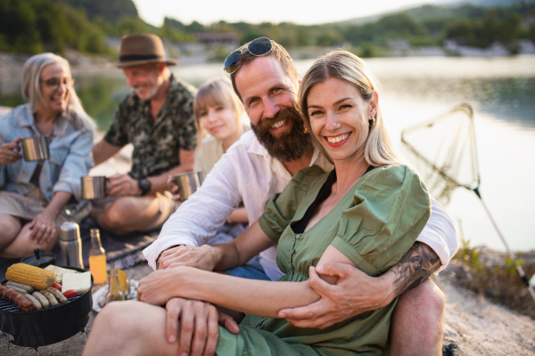 A happy multigeneration family on summer holiday trip, barbecue by lake.