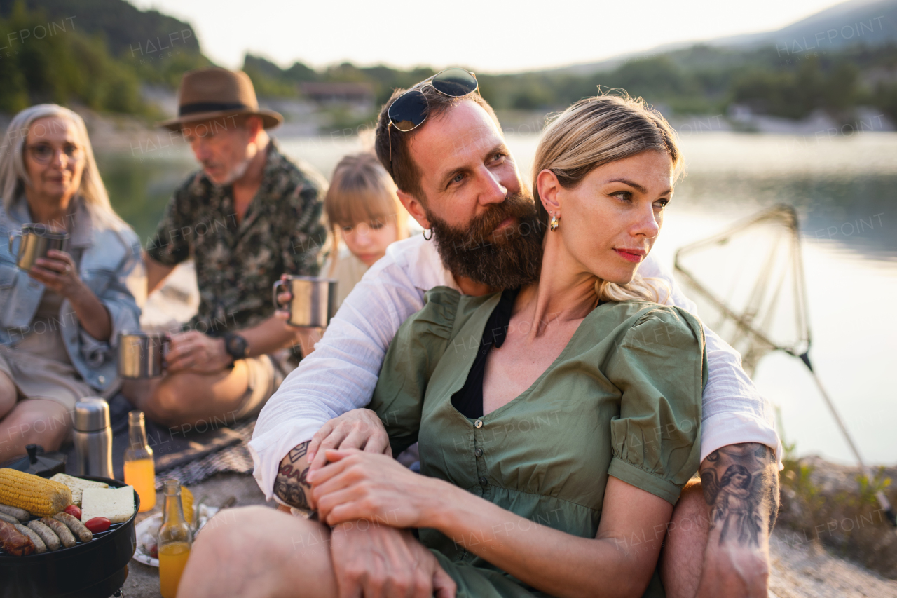 A happy multigeneration family on summer holiday trip, barbecue by lake.