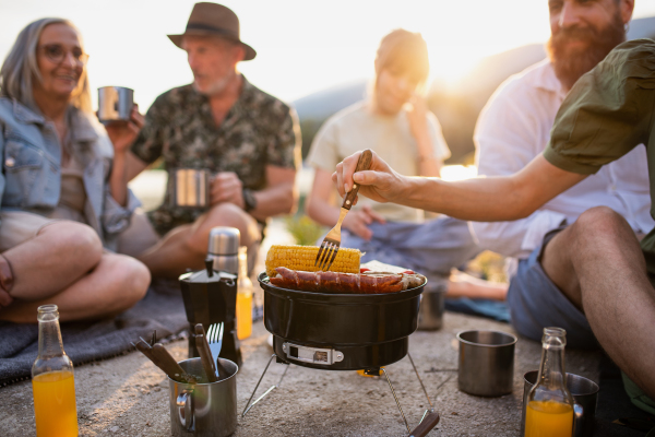 A happy multigeneration family on summer holiday trip, barbecue by lake.