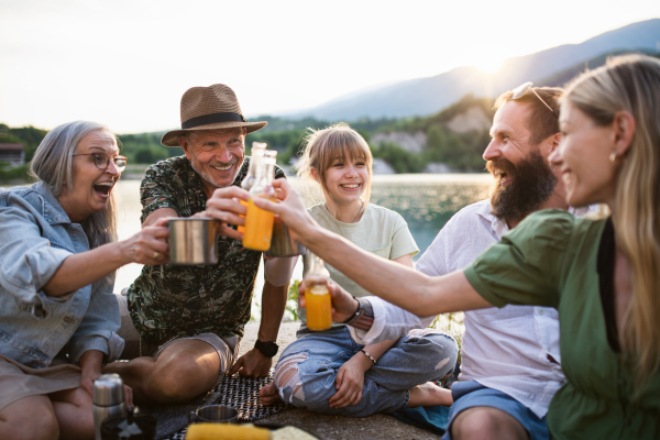 A happy multigeneration family on summer holiday trip, barbecue by lake.