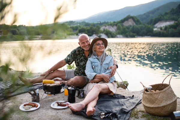 Portrait of happy senior couple resting on summer holiday trip, barbecue by lake.