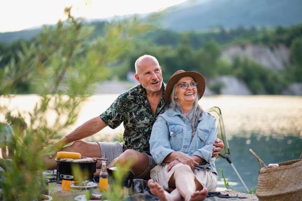 Portrait of happy senior couple resting on summer holiday trip, barbecue by lake.