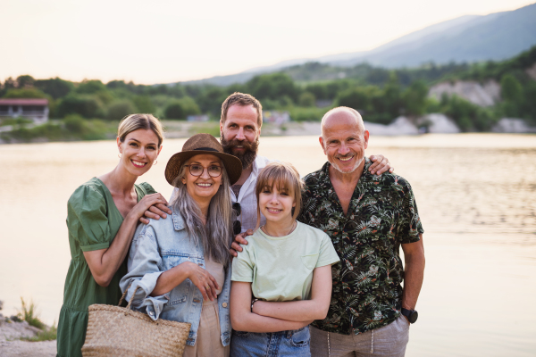 A happy multigeneration family on walk by lake on summer holiday, looking at camera.