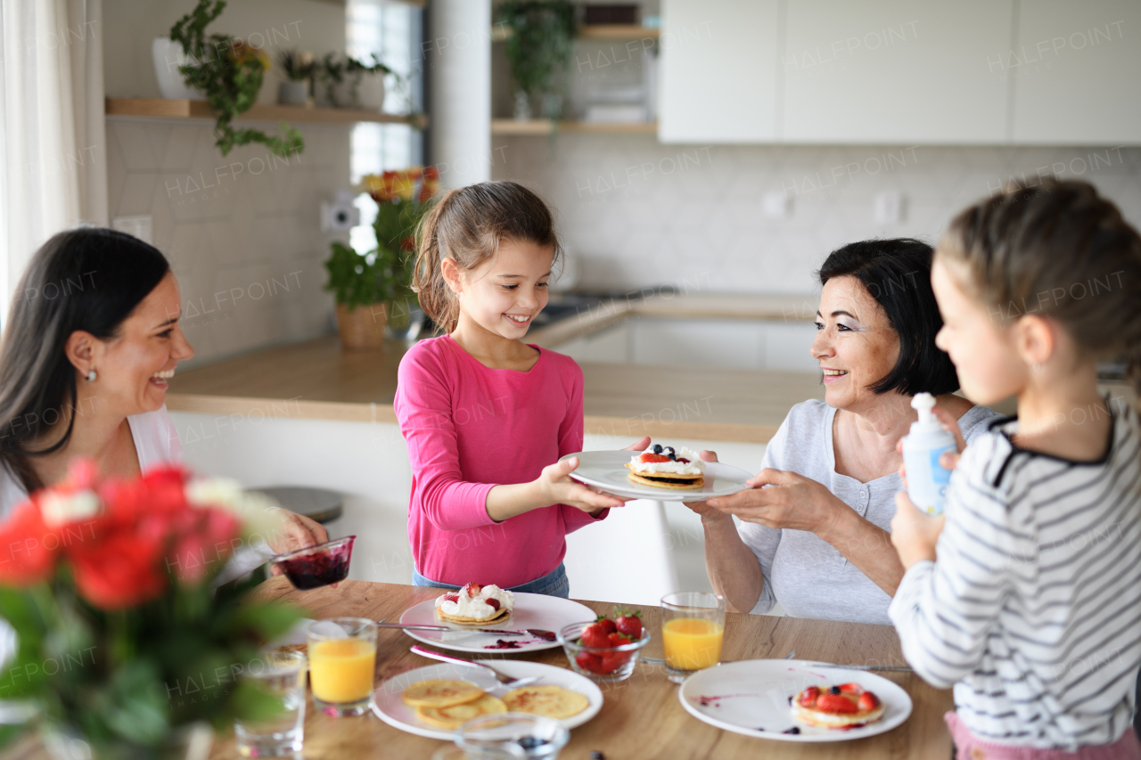 Happy small girls with mother and grandmother eating pancakes indoors at home, having a lunch.