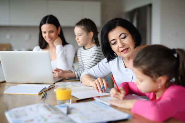 Happy small girls with mother and grandmother using a laptop indoors at home, home office and homework concept.