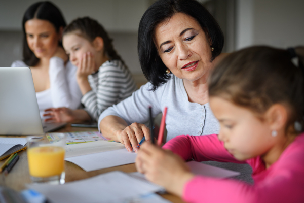 Happy small girls with a mother and grandmother doing homework using laptop indoors at home.