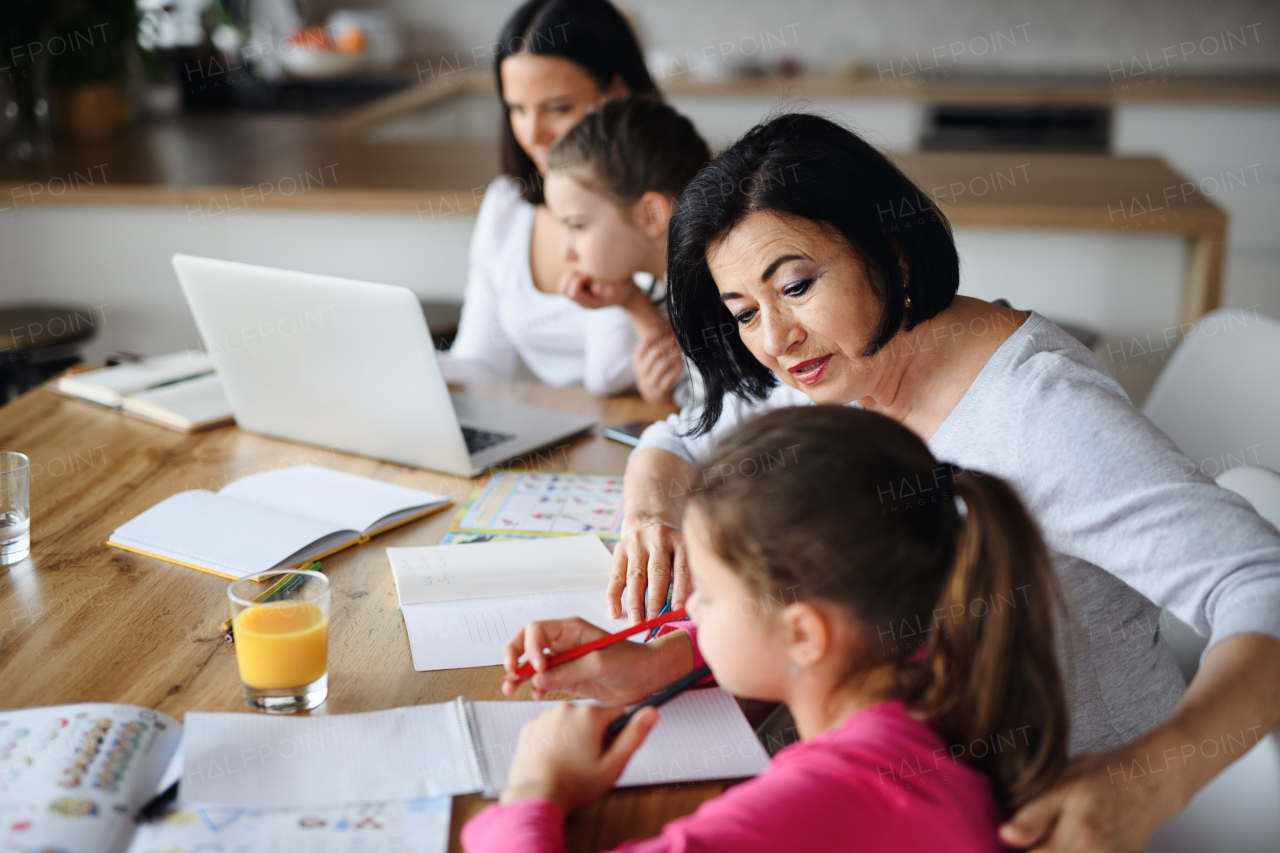 Happy small sisters with mother and grandmother doing homework using laptop indoors at home, home office and homeschool concept.