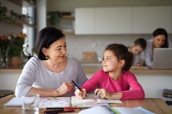 A small girl with grandmother doing homework indoors at home.