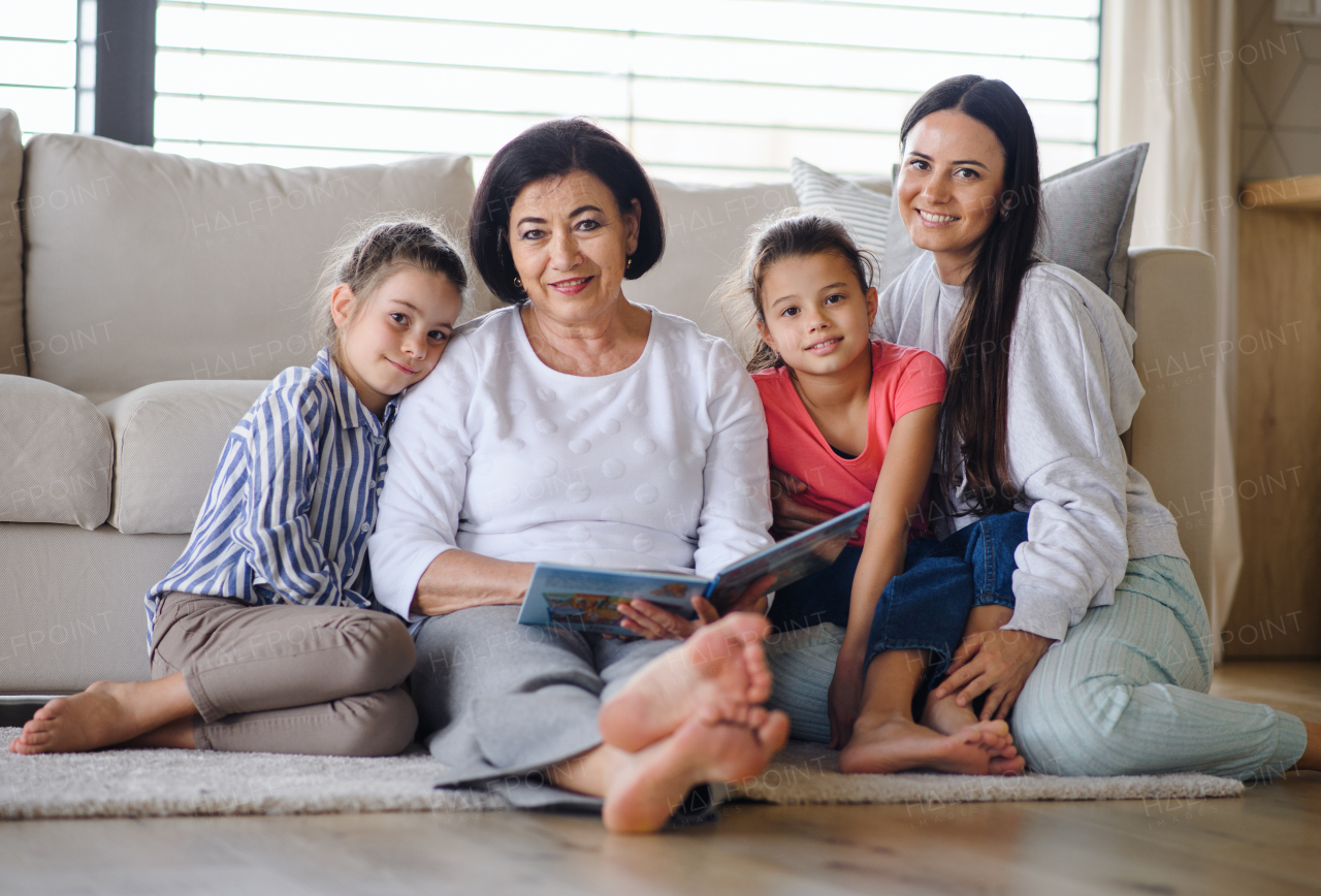 Happy small girls with a mother and grandmother indoors at home, sitting on floor and looking at camera