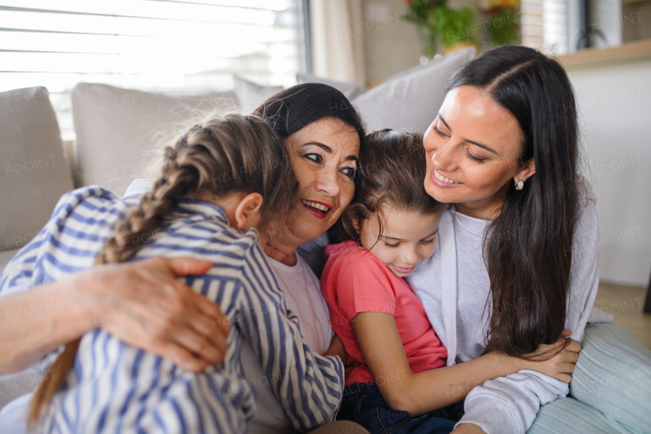 Portrait of happy small girls with mother and grandmother indoors at home, hugging.