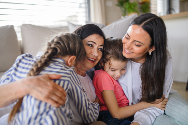 Portrait of happy small girls with mother and grandmother indoors at home, hugging.