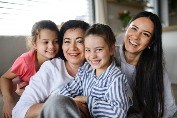 Happy small girls with a mother and grandmother indoors at home, sitting on floor and looking at camera