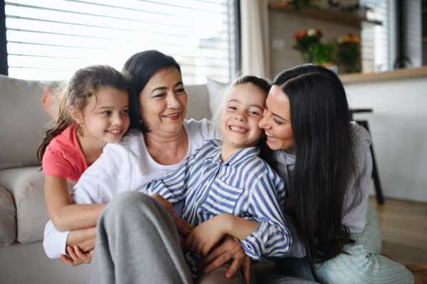 Portrait of happy small girls with mother and grandmother indoors at home, hugging.