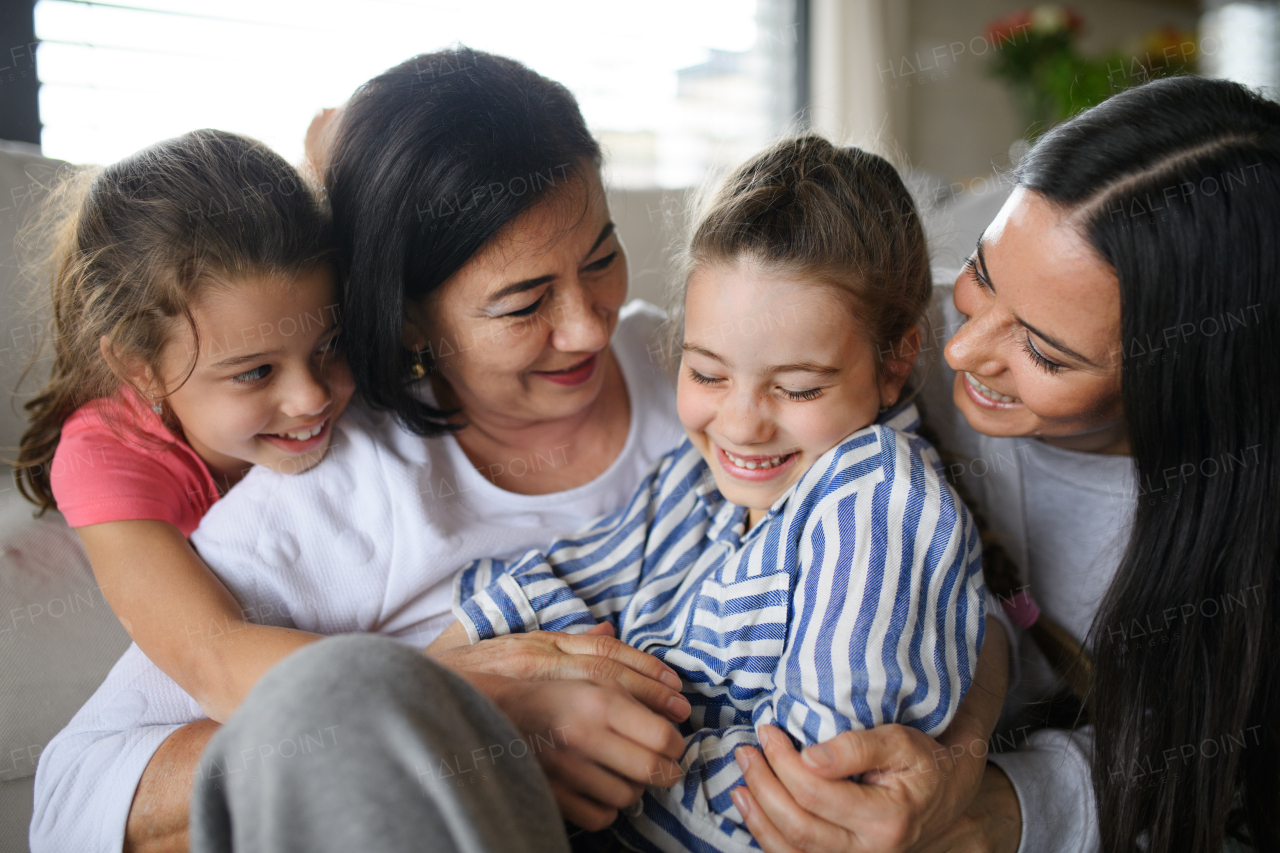 Portrait of happy small girls with mother and grandmother indoors at home, hugging.