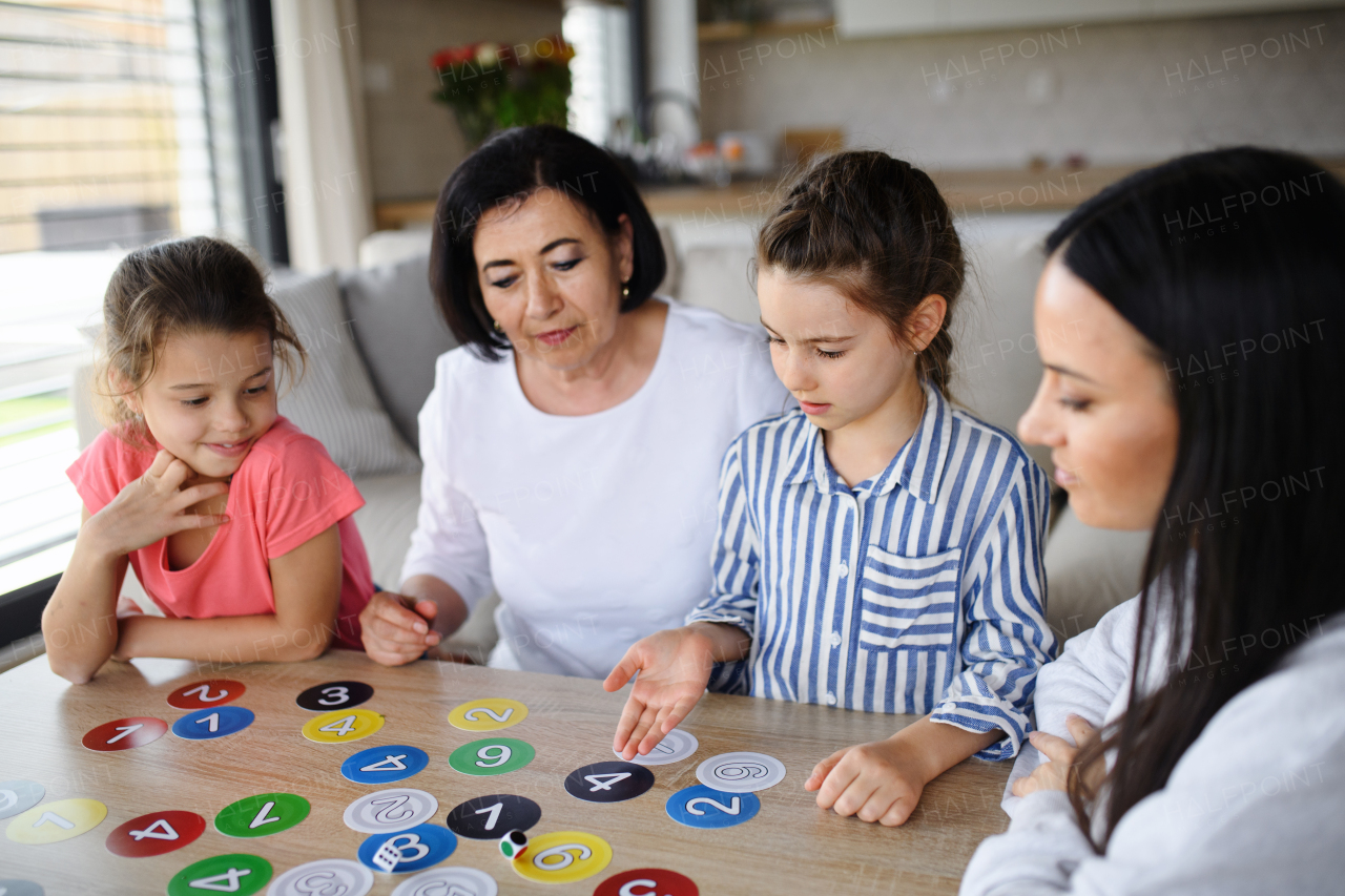 Happy small girls with a mother and grandmother playing cards indoors at home.