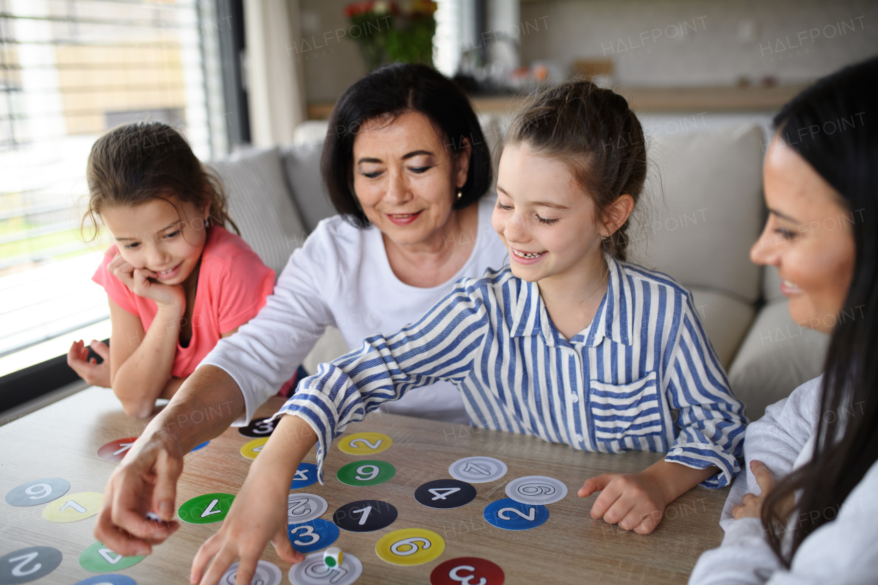 Happy small girls with a mother and grandmother playing cards indoors at home.