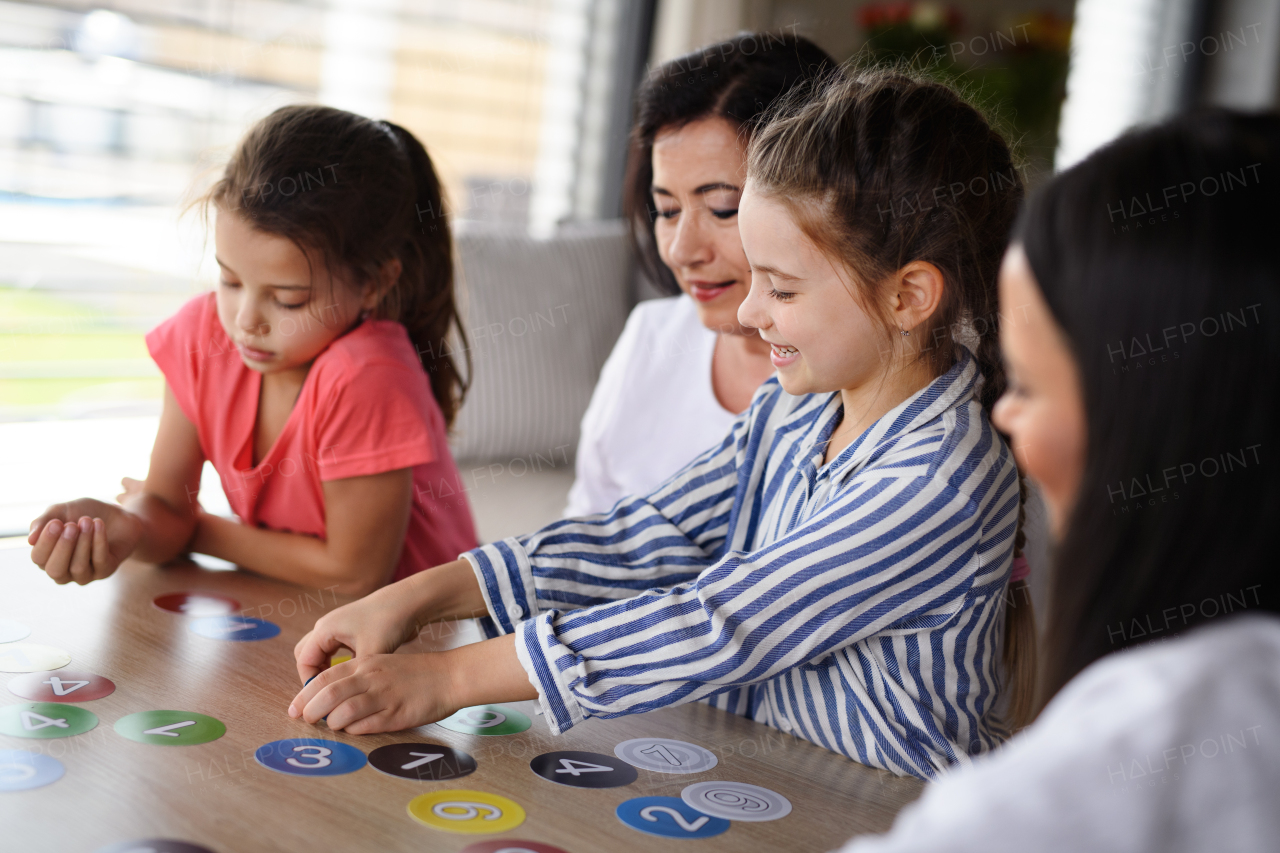 Happy small girls with a mother and grandmother playing cards indoors at home.