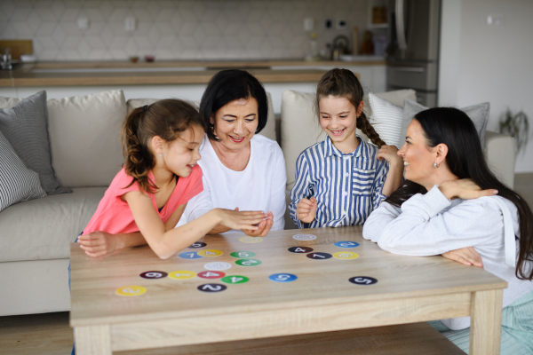 Happy small girls with a mother and grandmother playing cards indoors at home.