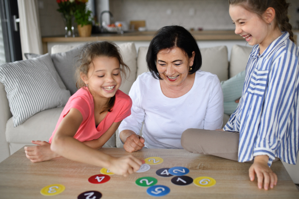 Happy small girls with a grandmother playing cards indoors at home.