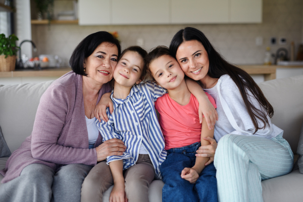 Portrait of happy small girls with mother and grandmother indoors at home, looking at camera.